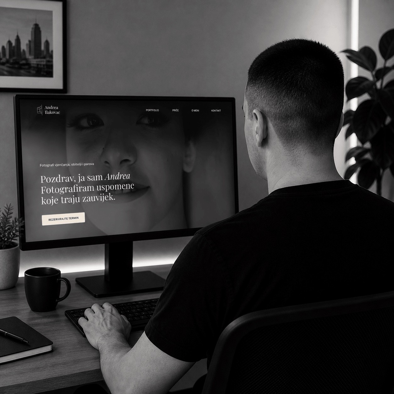 A man sits at a desk working on a laptop, focused, with books and a lamp in the background.